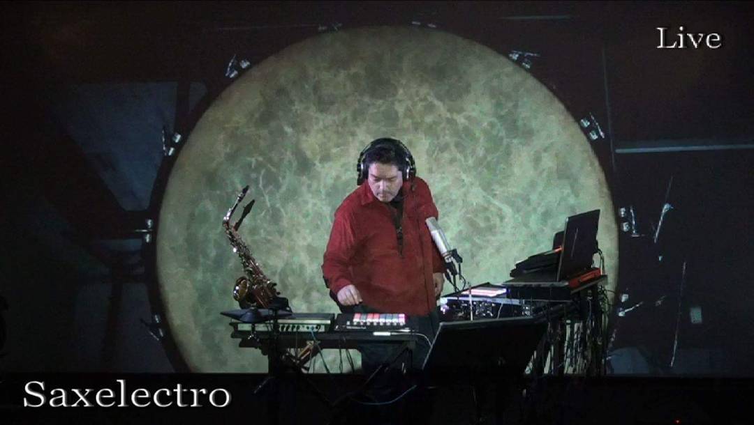 Andreas at his live rig, saxophone on its stand, in front of a projected moon